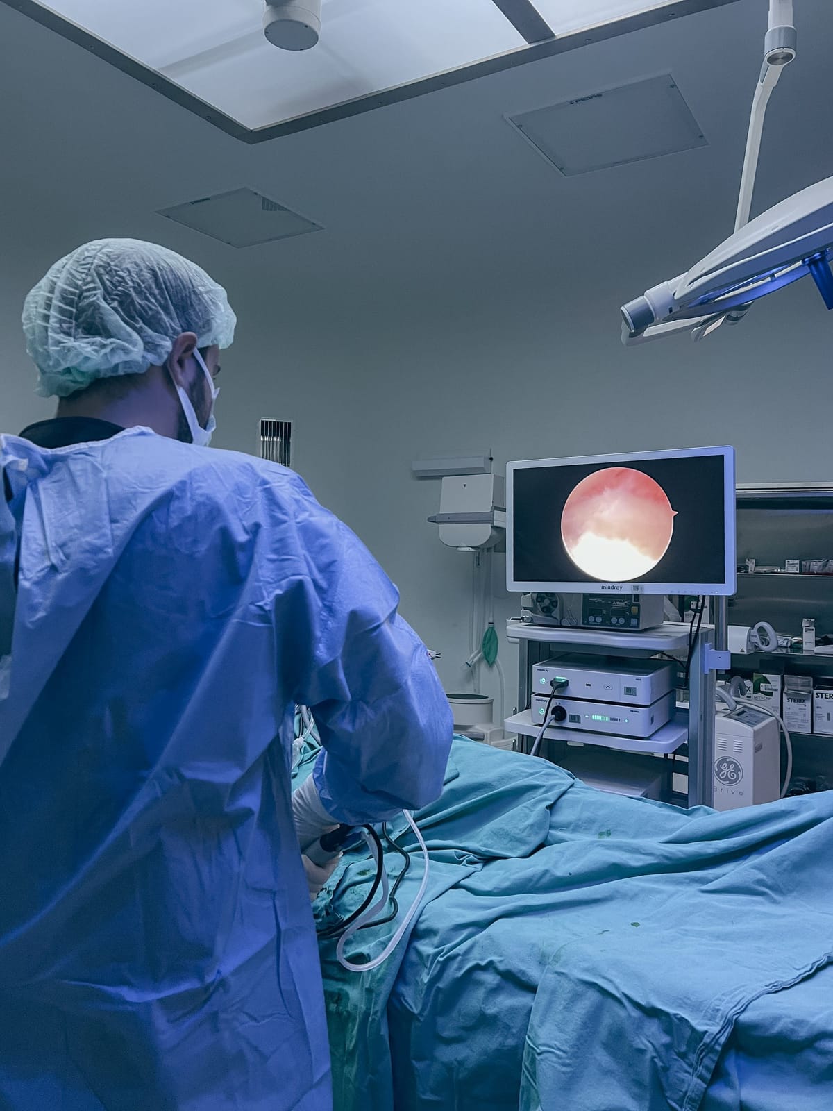 Surgeon in a blue disposable gown and bouffant cap at the operating table in a modern theatre