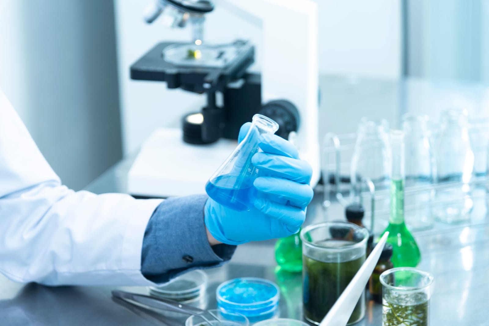 Scientist in blue gloves holding a flask of blue liquid at a laboratory bench