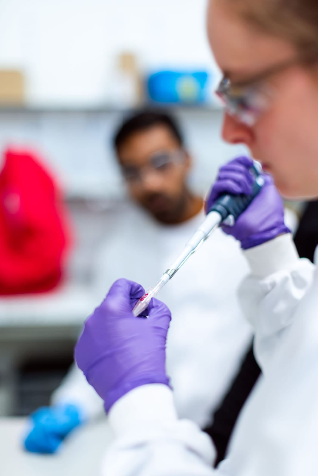 Scientist in safety glasses and purple gloves using a micropipette in a laboratory